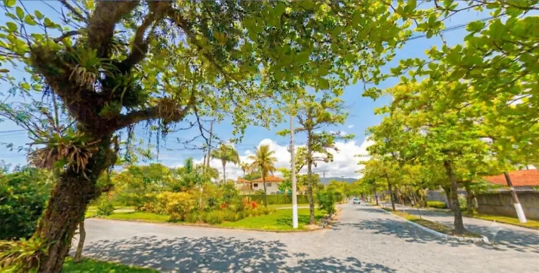 Rua arborizada em área residencial do Guarujá, com casas de baixo perfil e vegetação abundante.