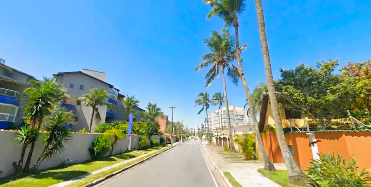 Rua arborizada em Bertioga, com palmeiras, jardins e construções de perfil baixo.